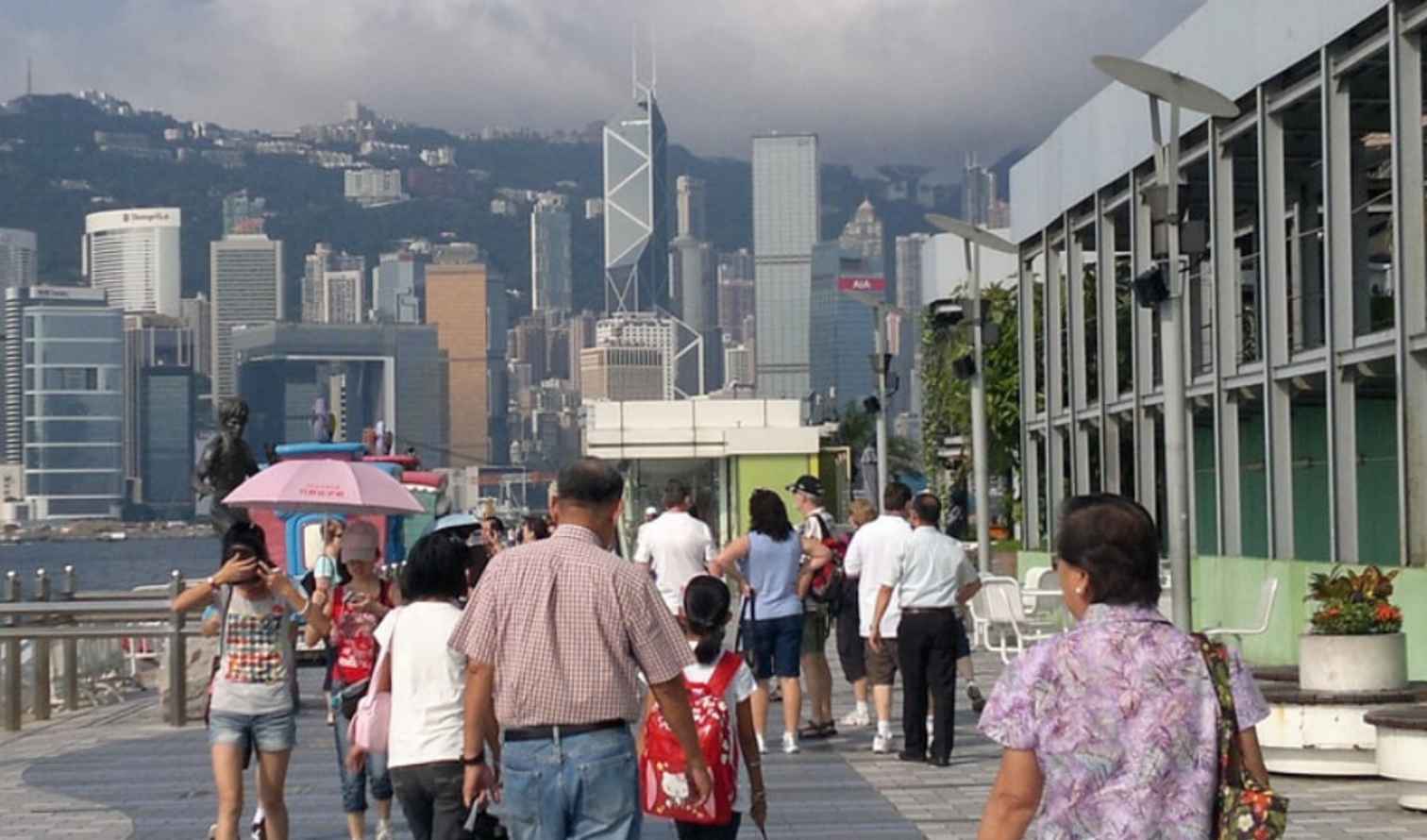 People walking along the promenade with Hong Kong skyline in the background.