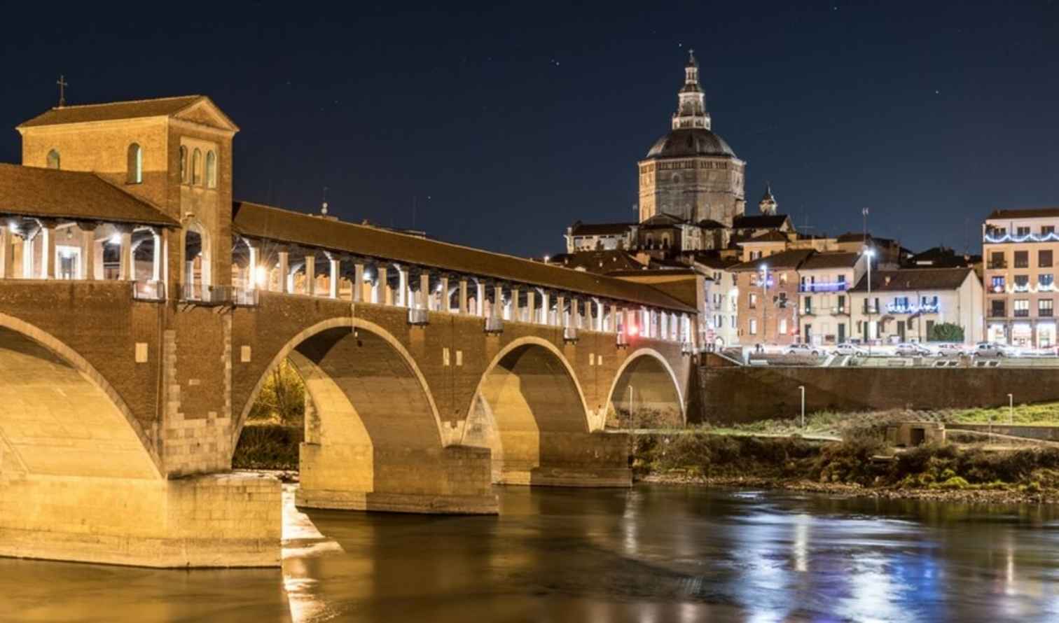 The Ponte Coperto bridge illuminated at night in Pavia, Italy.