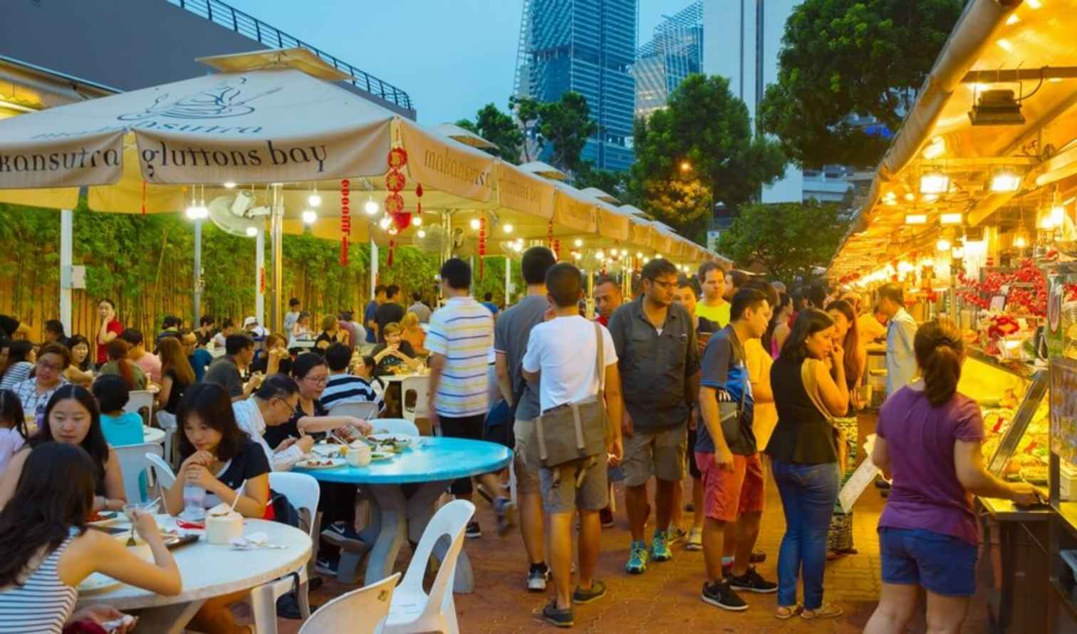 Crowd enjoying meals under umbrellas at a Singapore food court.