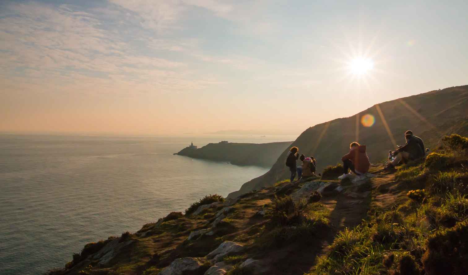 Backlit hikers resting on Howth Head, overlooking Dublin Bay and Baily Lighthouse.