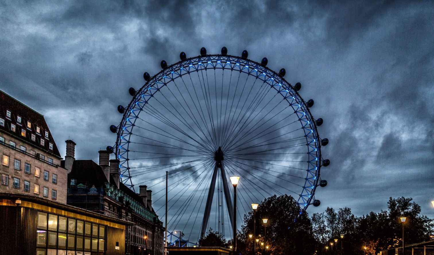 People walk near the London Eye on a cloudy evening.