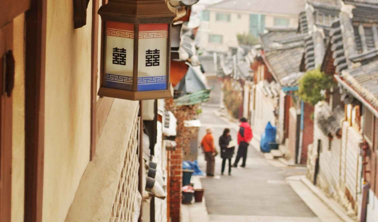 Three people walking down an alley in Bukchon Hanok Village, Seoul.