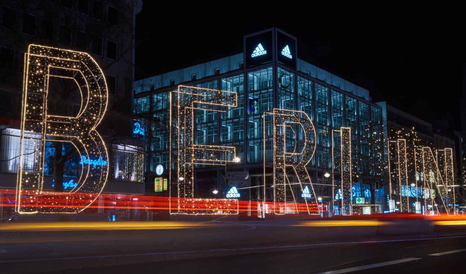 Illuminated Berlin sign in front of an Adidas store at night.