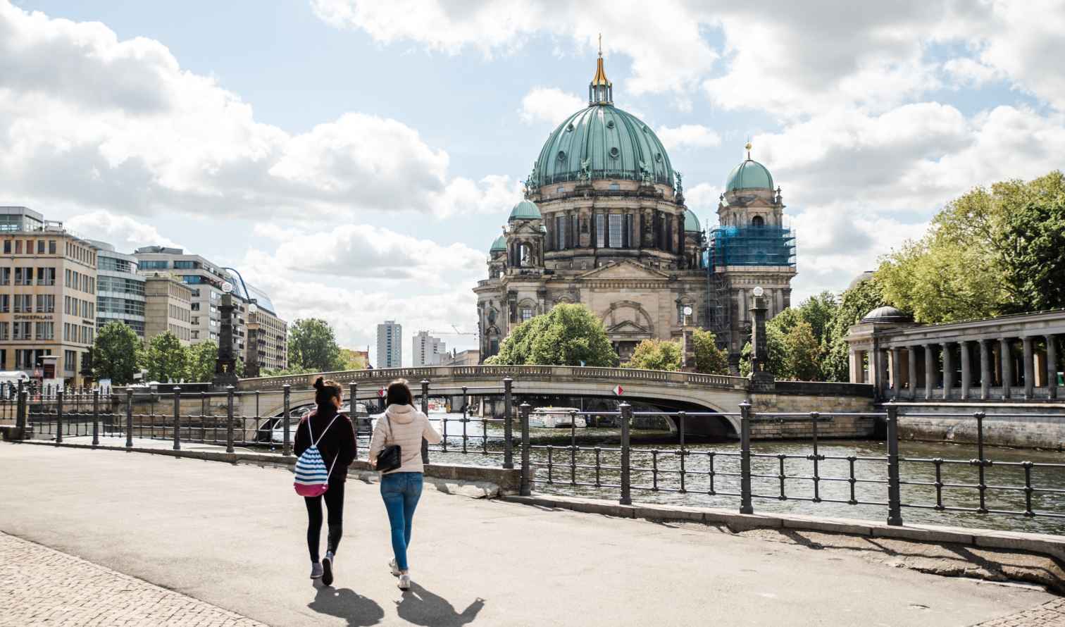 Two people walking towards Berlin Cathedral along the riverbank.