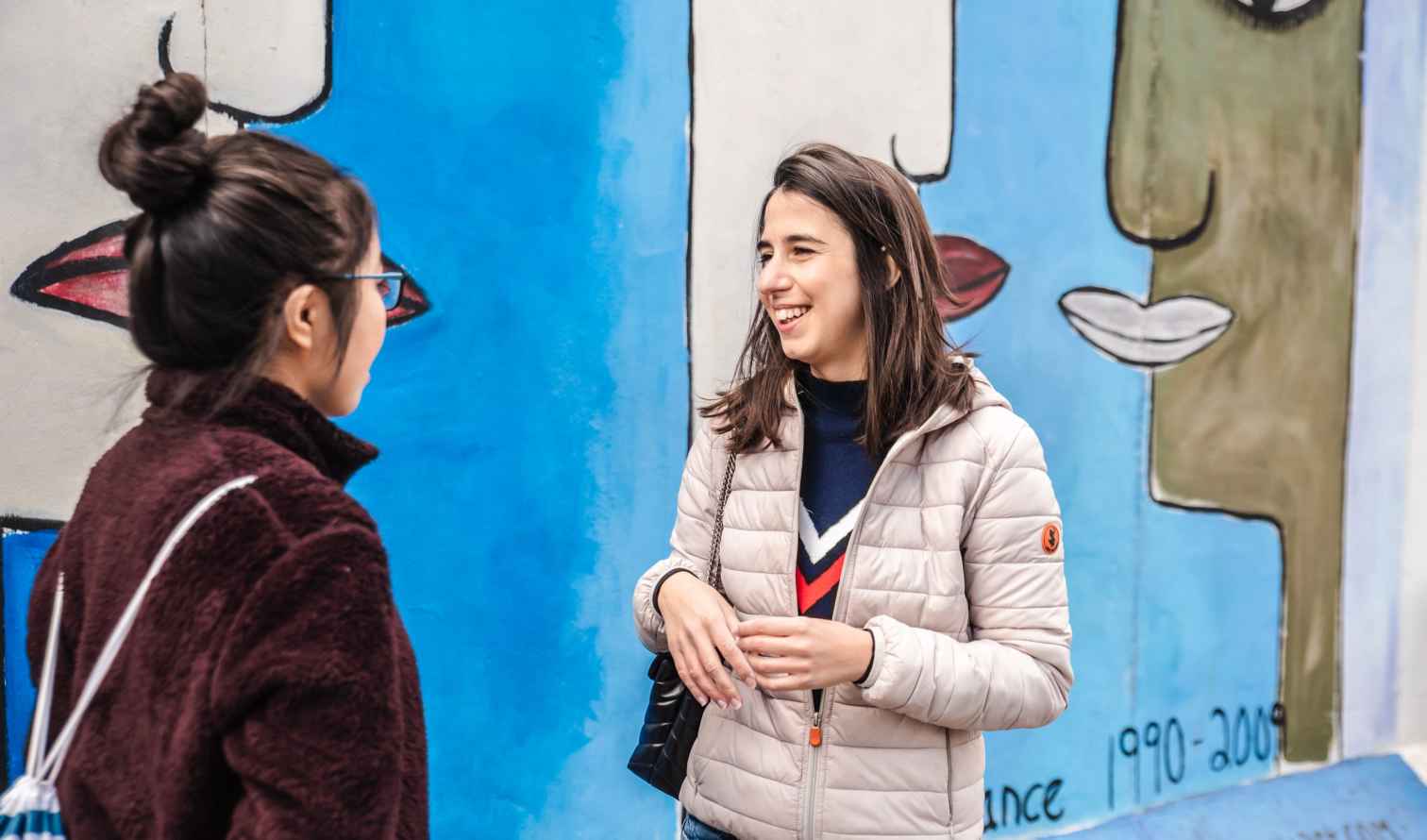 Two women standing in front of a colorful mural by Mary Mackey in Berlin