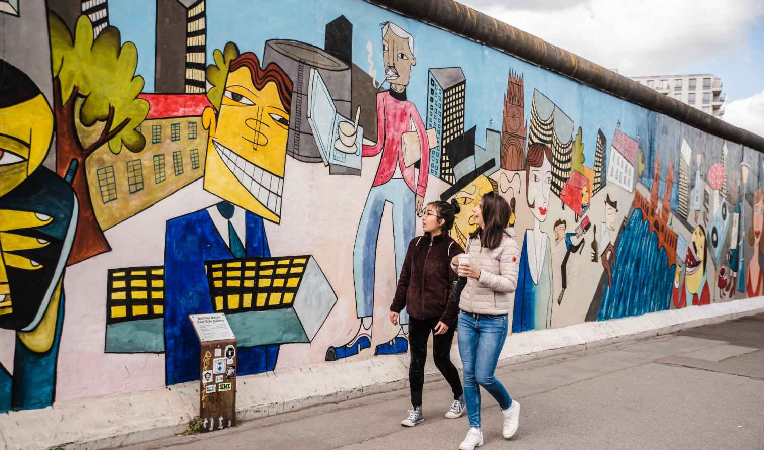 Two people walking by the Berlin Wall mural.