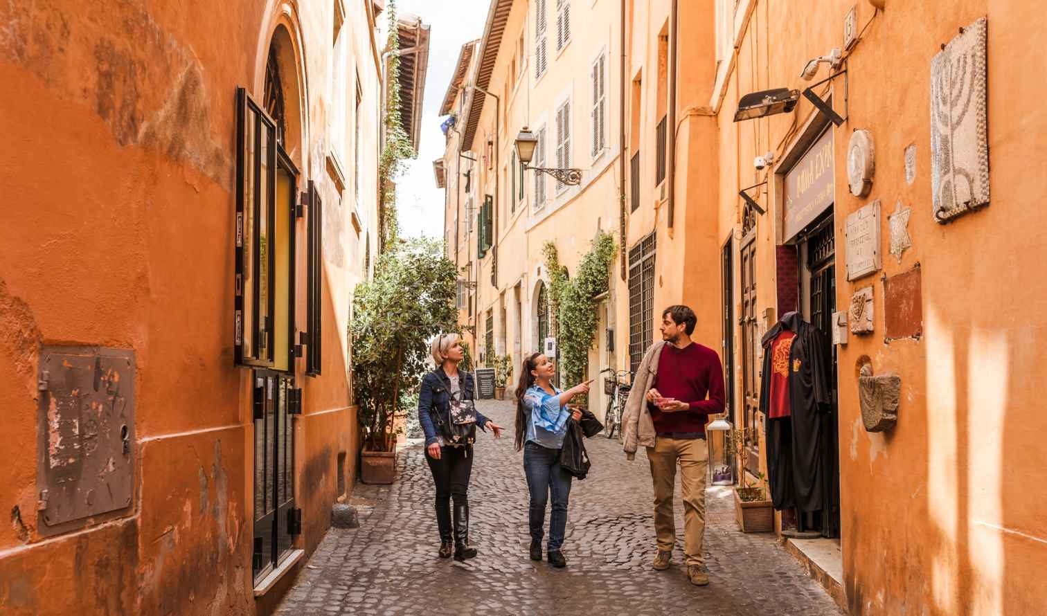 Three people walking on a cobblestone street in Rome, Italy.
