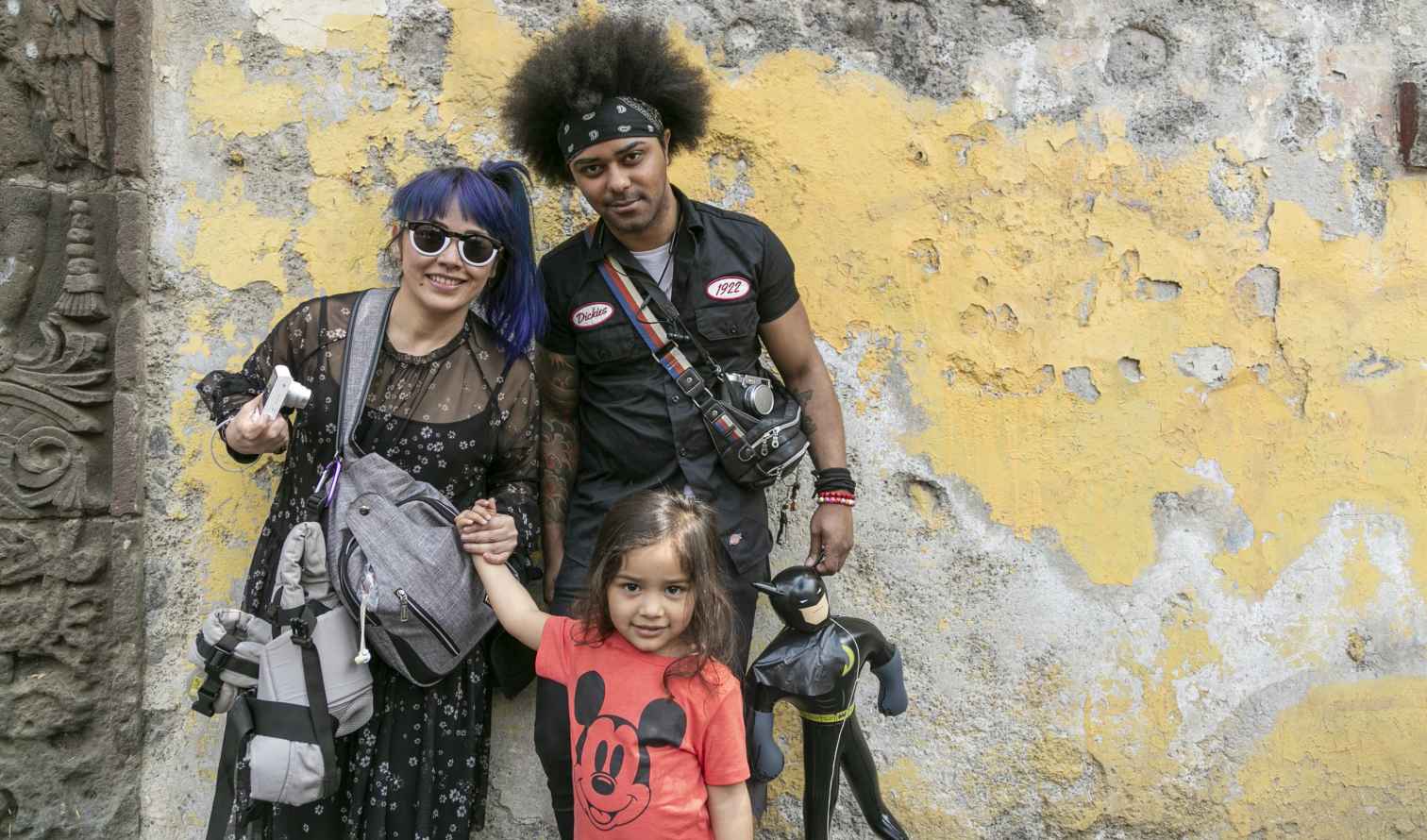 Three people pose beside a weathered yellow wall with Aztec carvings in Mexico