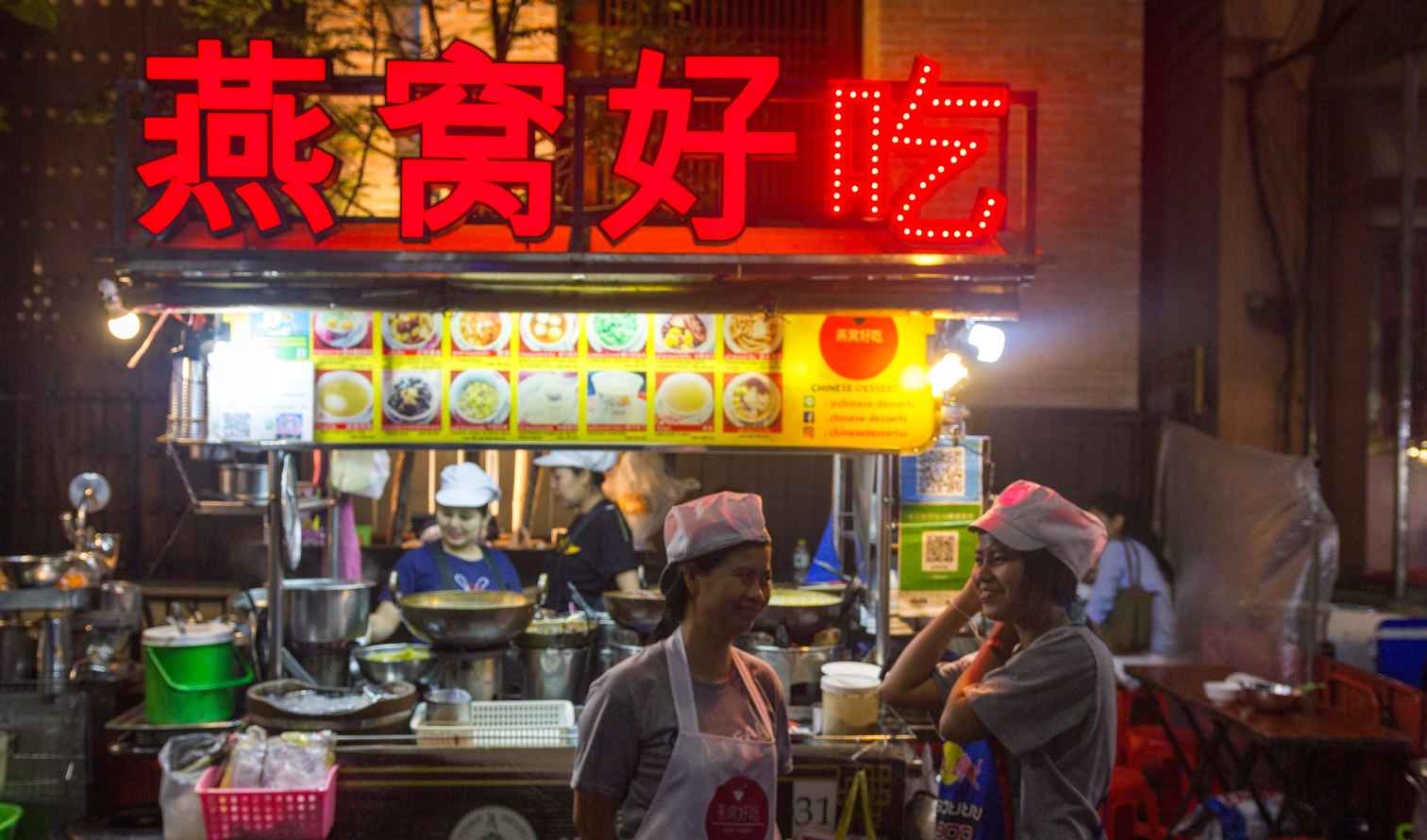 Street food stall with a red Chinese sign at night in Bangkok.