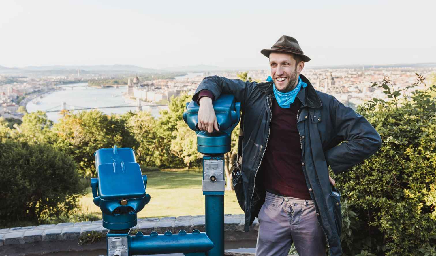Man standing by a blue telescope at a Budapest viewpoint.