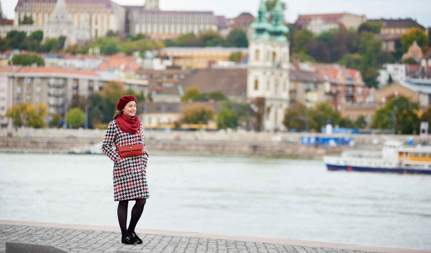 Individual wearing a red beret and coat by Budapest's Danube River.