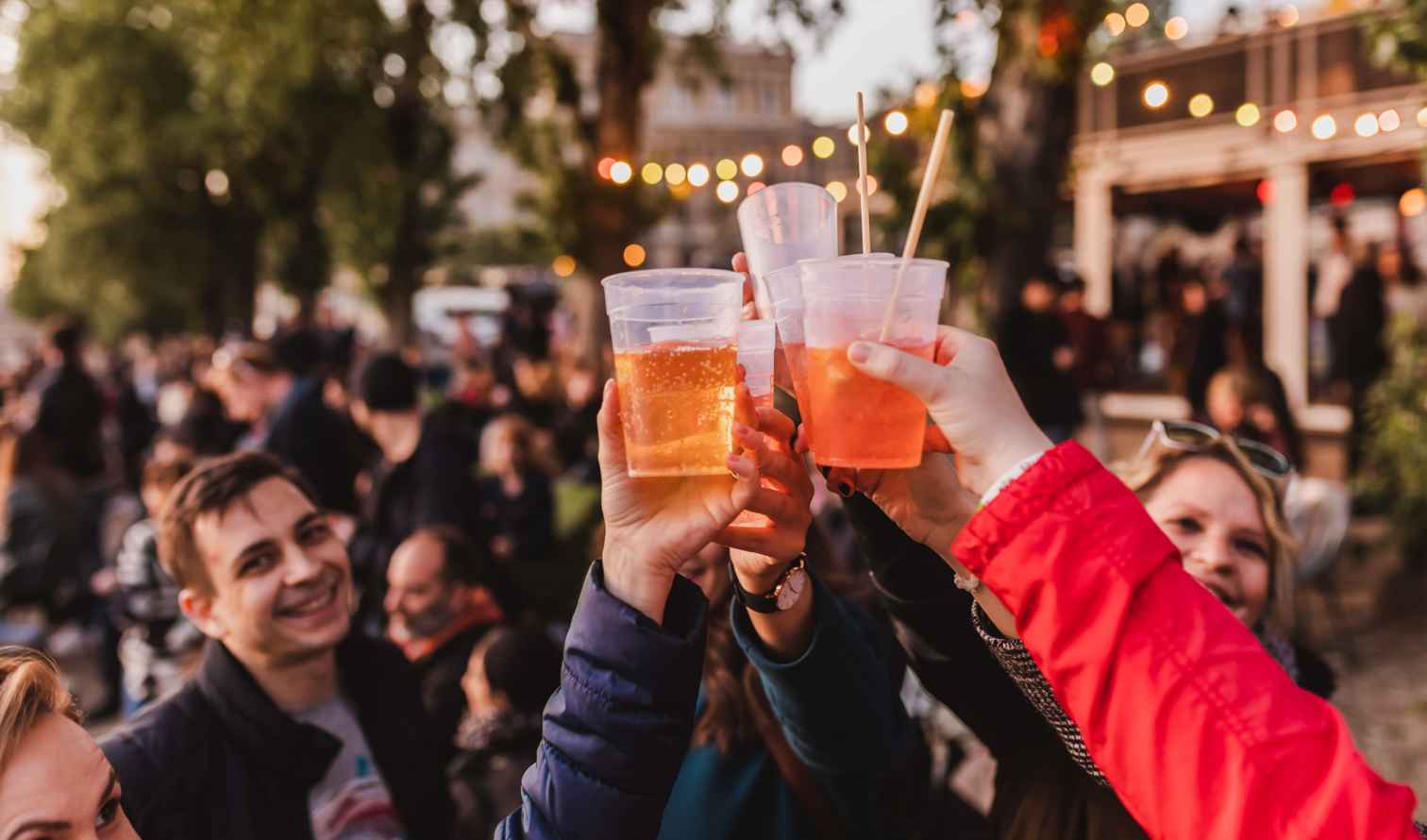 People raising plastic cups outdoors with a crowd in the background in Budapest