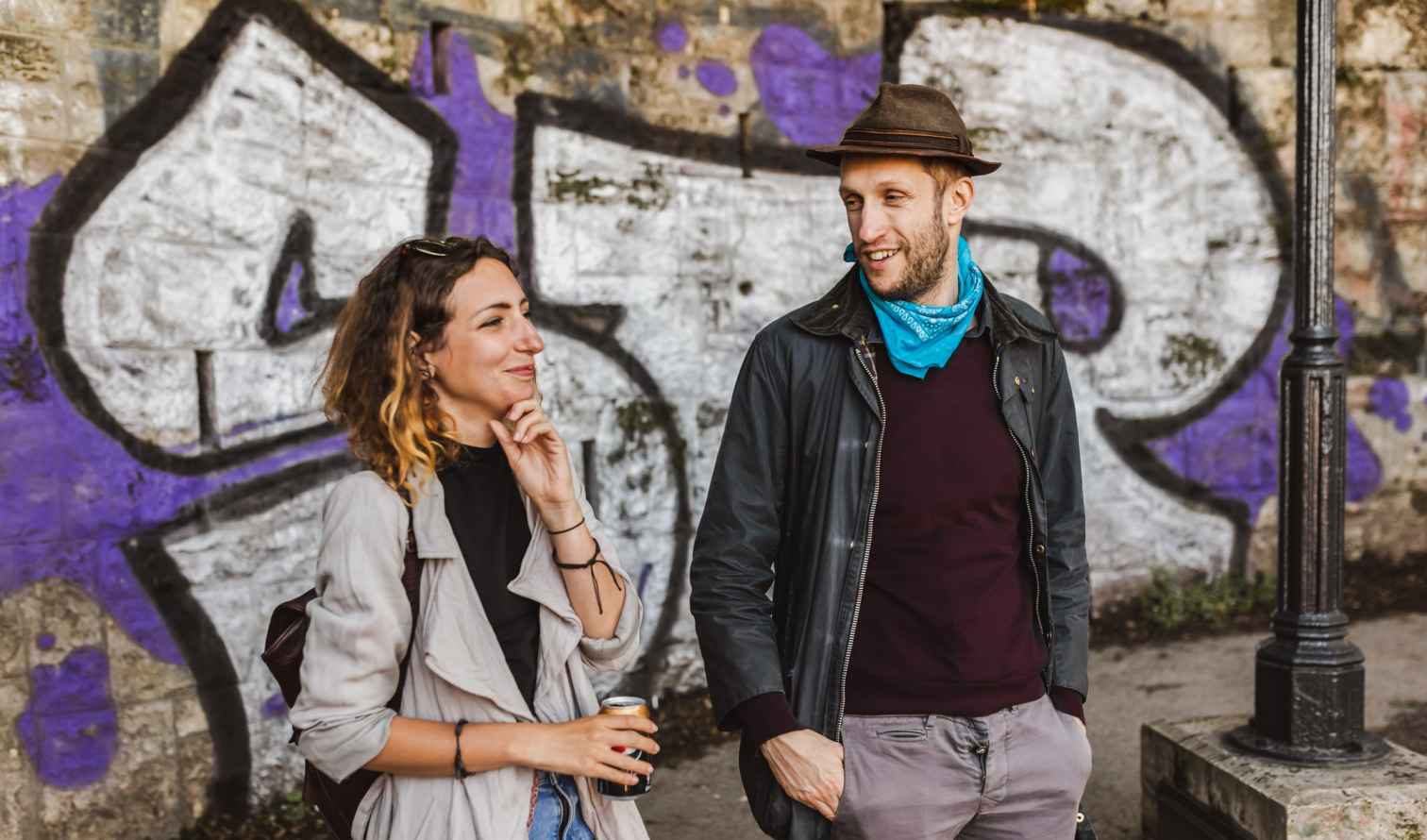 Casually dressed couple conversing by a wall adorned with graffiti in Budapest