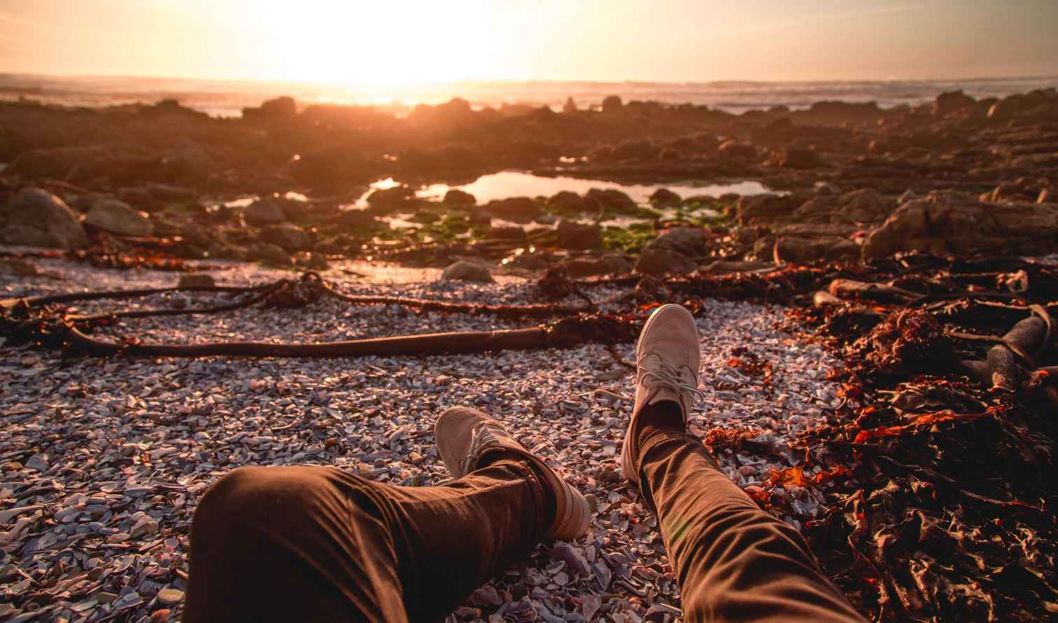 Person sitting on a rocky beach looking at the sunset in Cape Town
