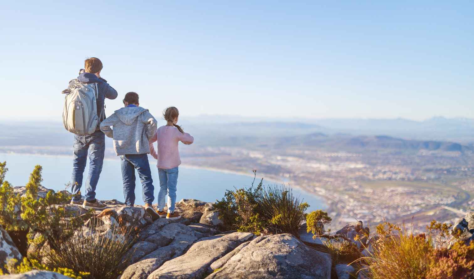 Three people stand on rocks overlooking Cape Town's coastline.