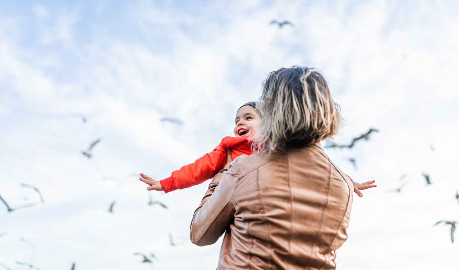 Woman with short hair holding a child outdoors with a blue sky in Istanbul