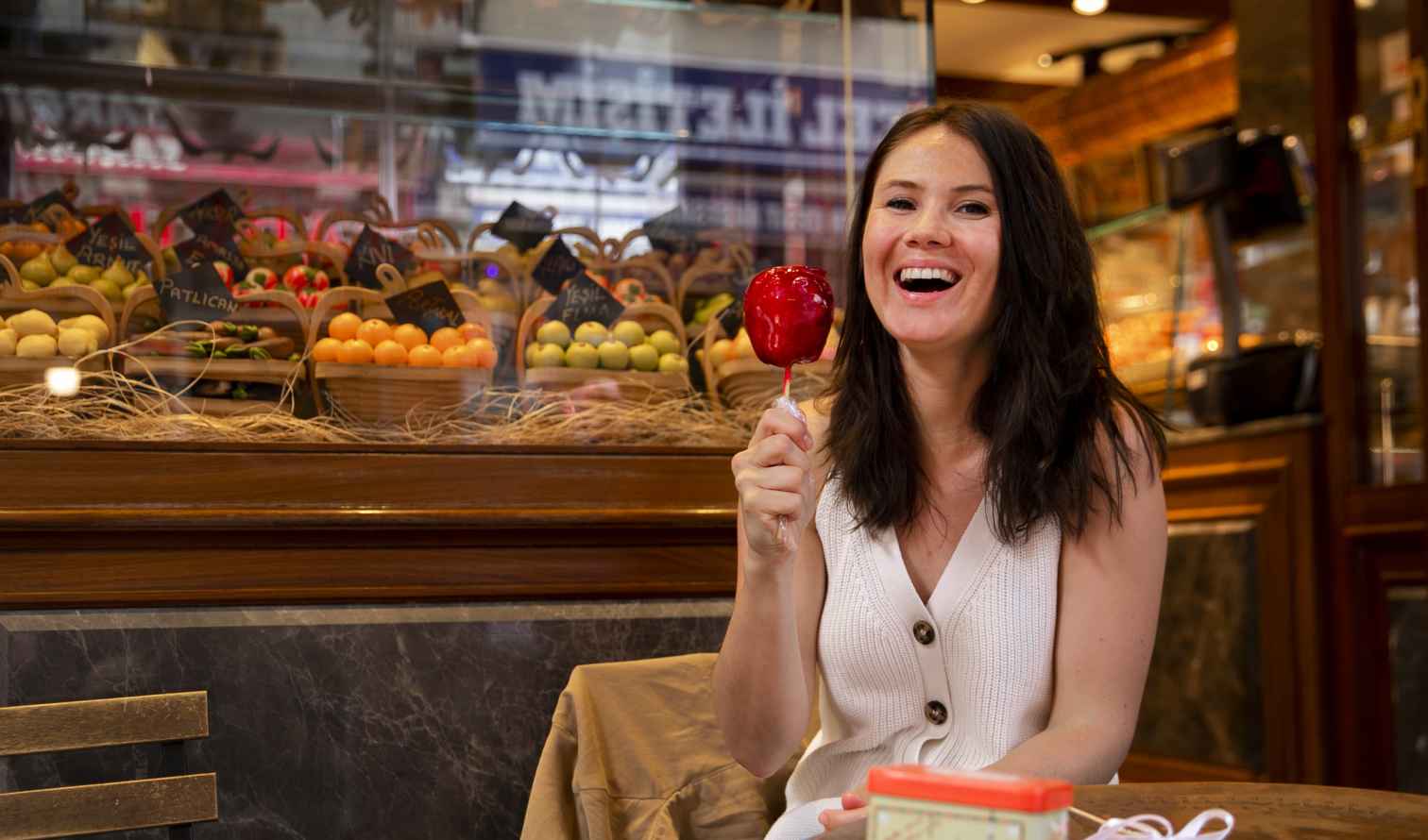 Woman holding a candy apple in front of a Turkish shop display.