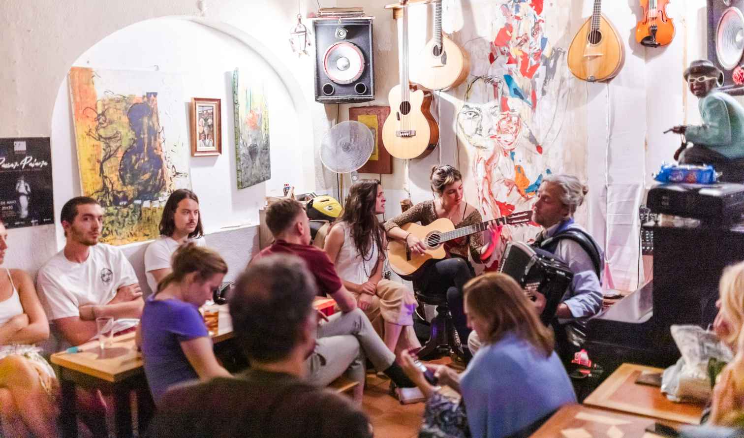 People gather for a music session in a cozy room with guitars and artwork in Lisbon