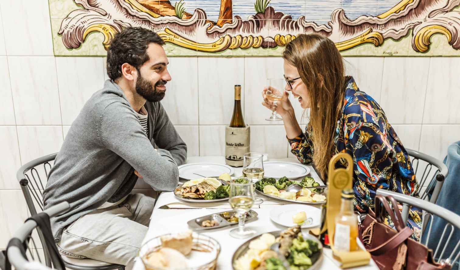 A man and woman enjoying a meal with wine at a small restaurant in Lisbon