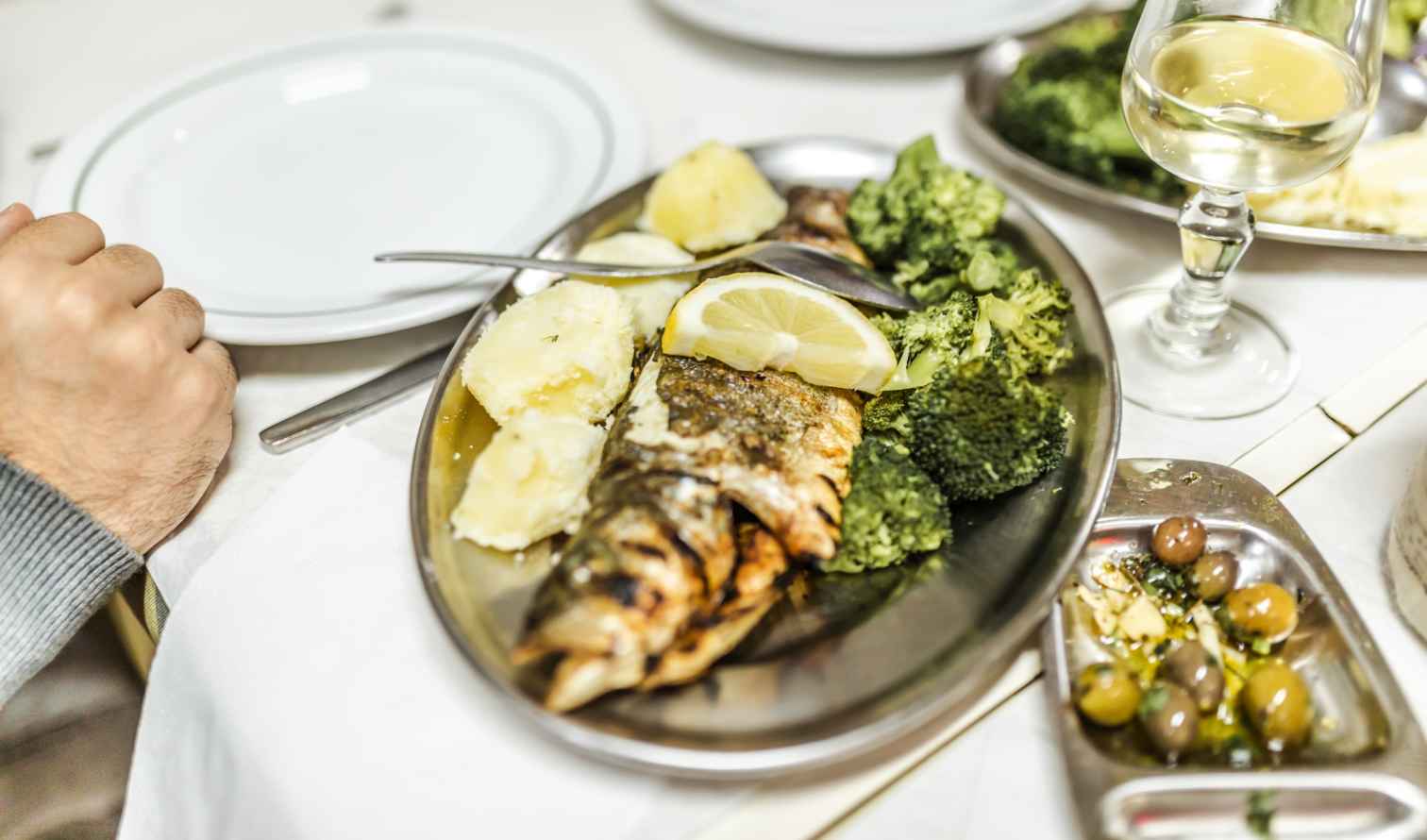 Grilled fish with lemon, broccoli, and potatoes on a metallic plate in Lisbon