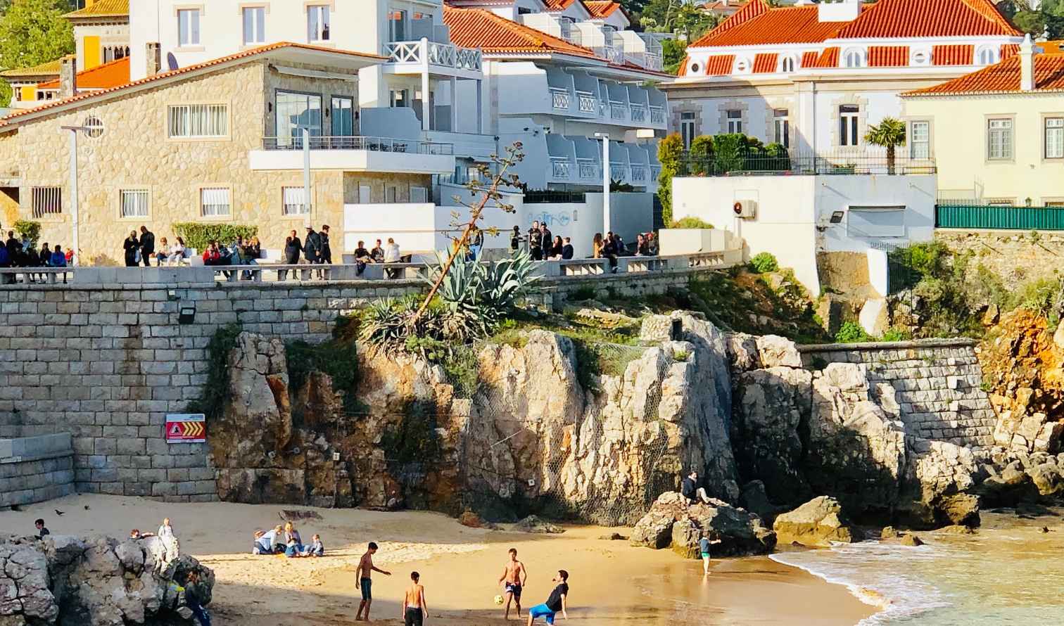 People playing soccer on a small beach in Cascais, Portugal beneath a stone wall.