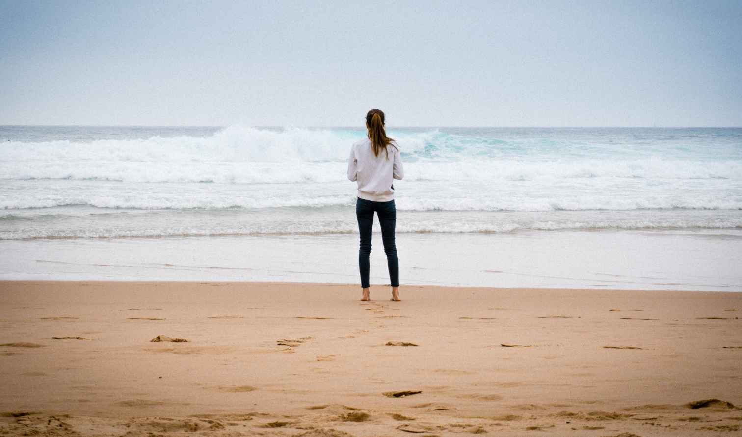 Person standing on a sandy beach looking at the ocean waves in Belem