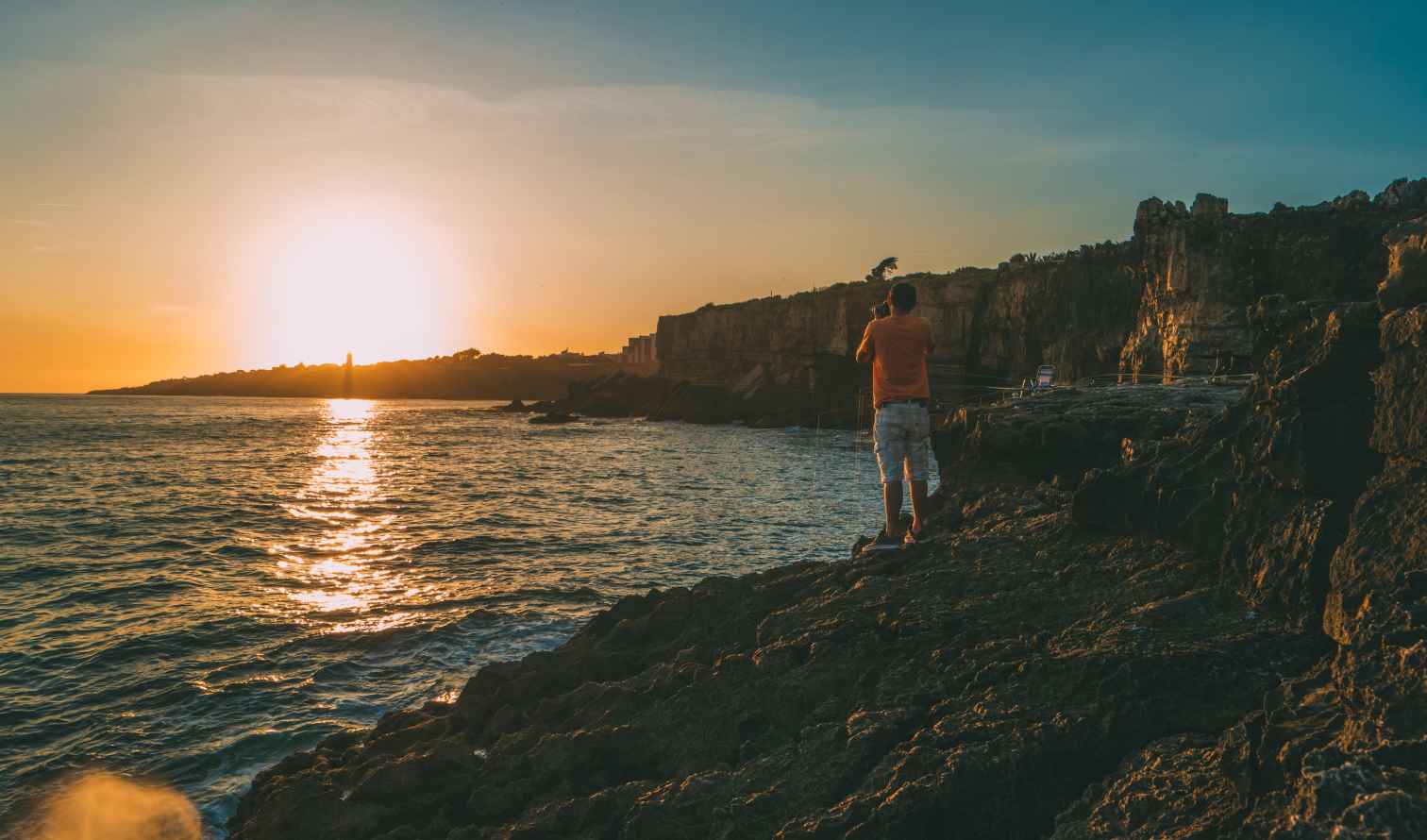 Person standing on rocky coast at sunset near Cascais, Portugal.