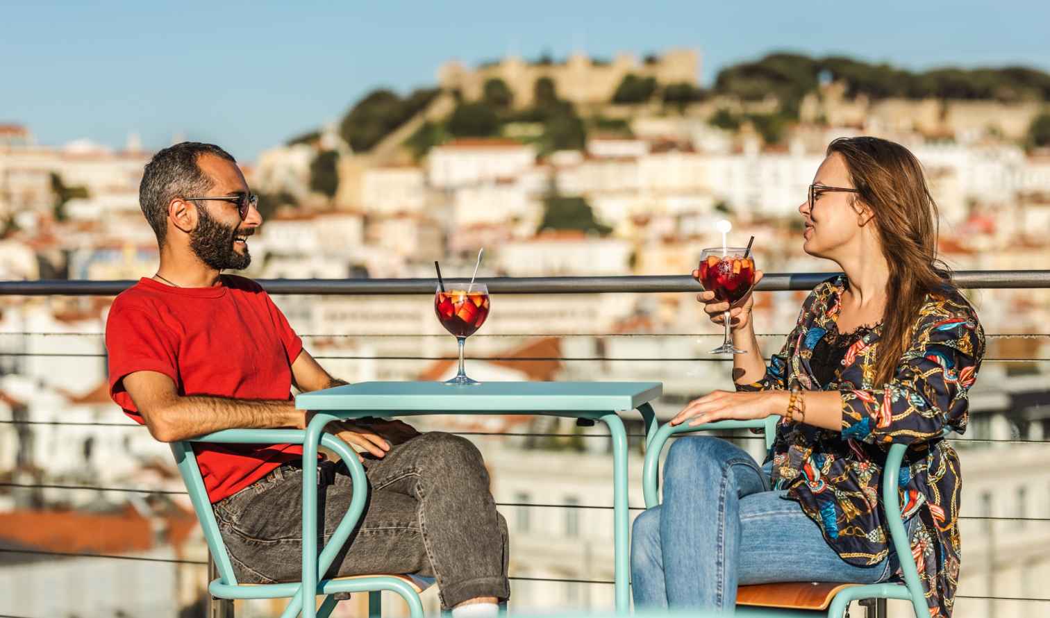 Two people sitting at a rooftop café overlooking Lisbon's São Jorge Castle.