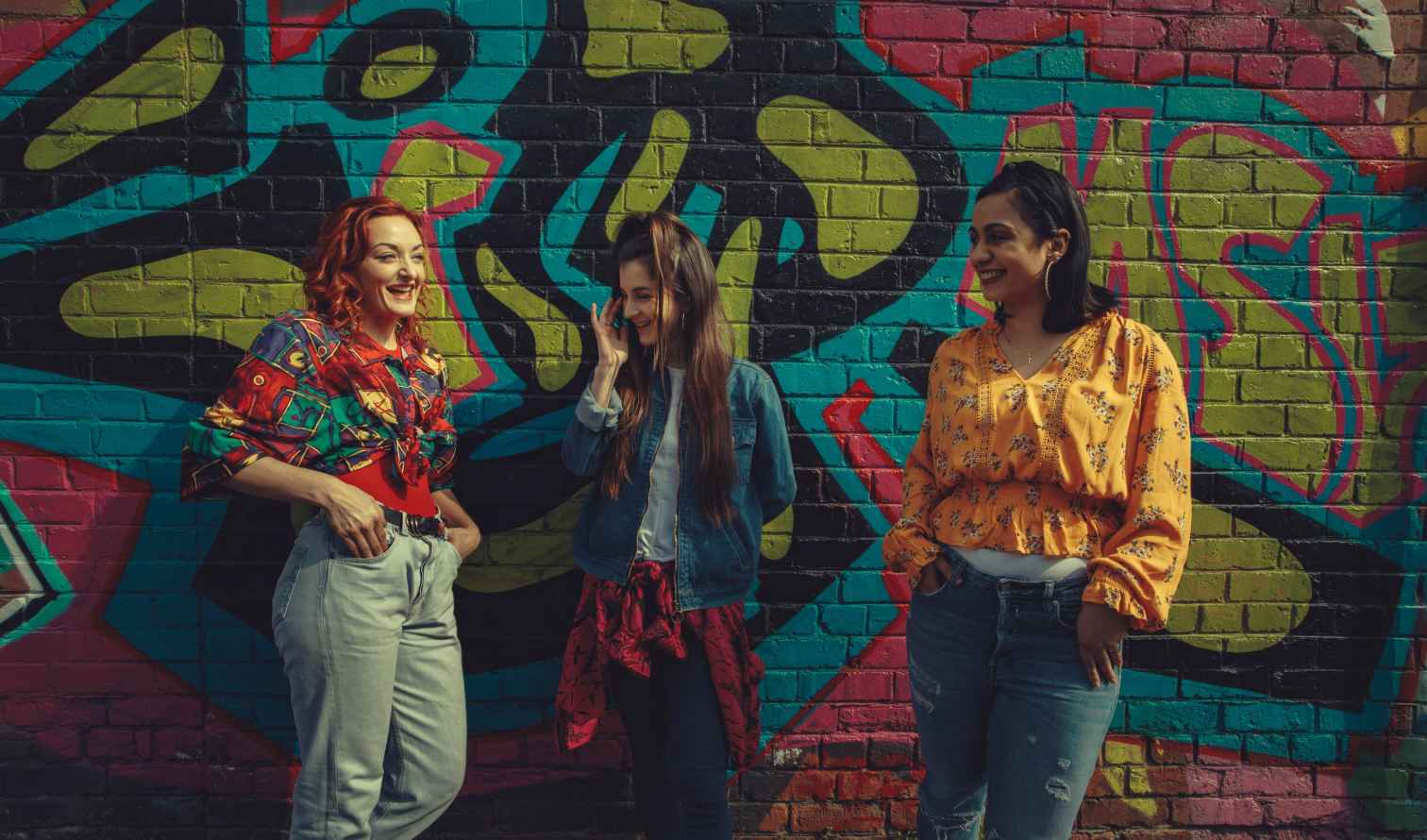 Three women standing in front of a colorful graffiti wall in Liverpool
