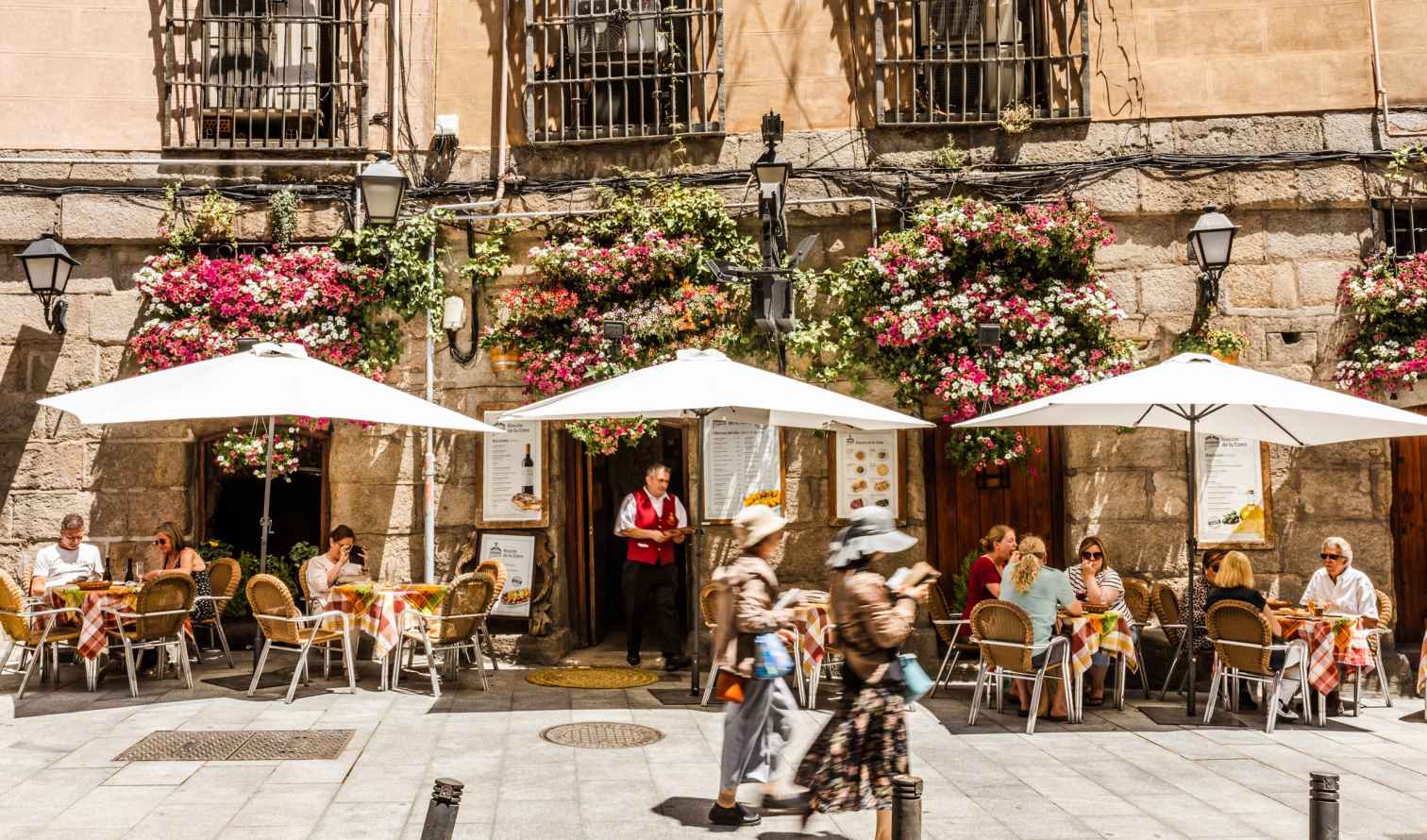 Outdoor cafe with white umbrellas and flower-covered walls in Madrid, Spain.