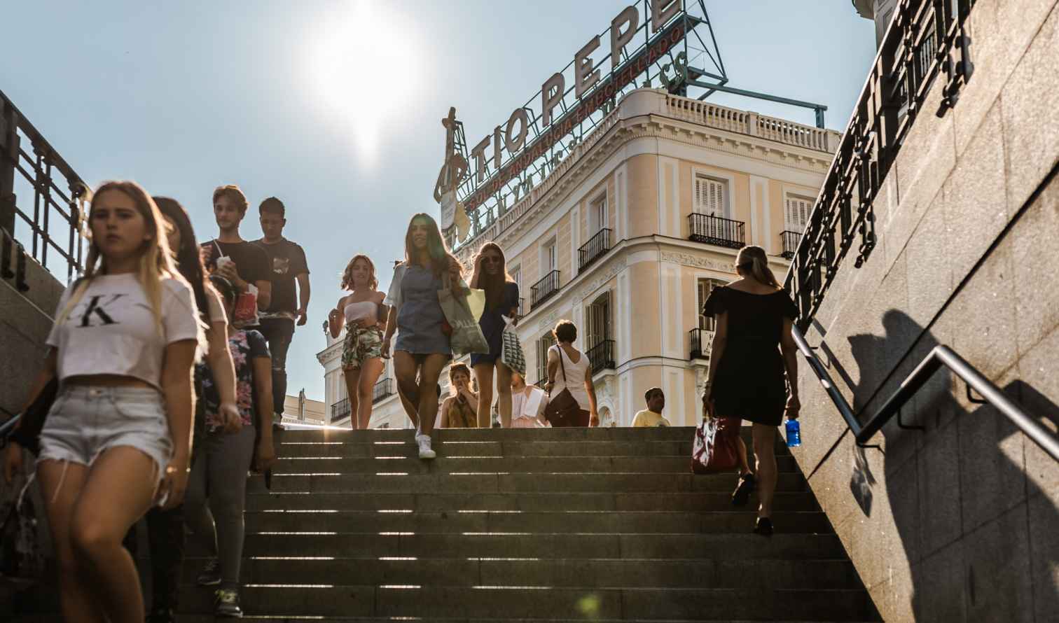 People walking down stairs near Tío Pepe sign in Puerta del Sol, Madrid.