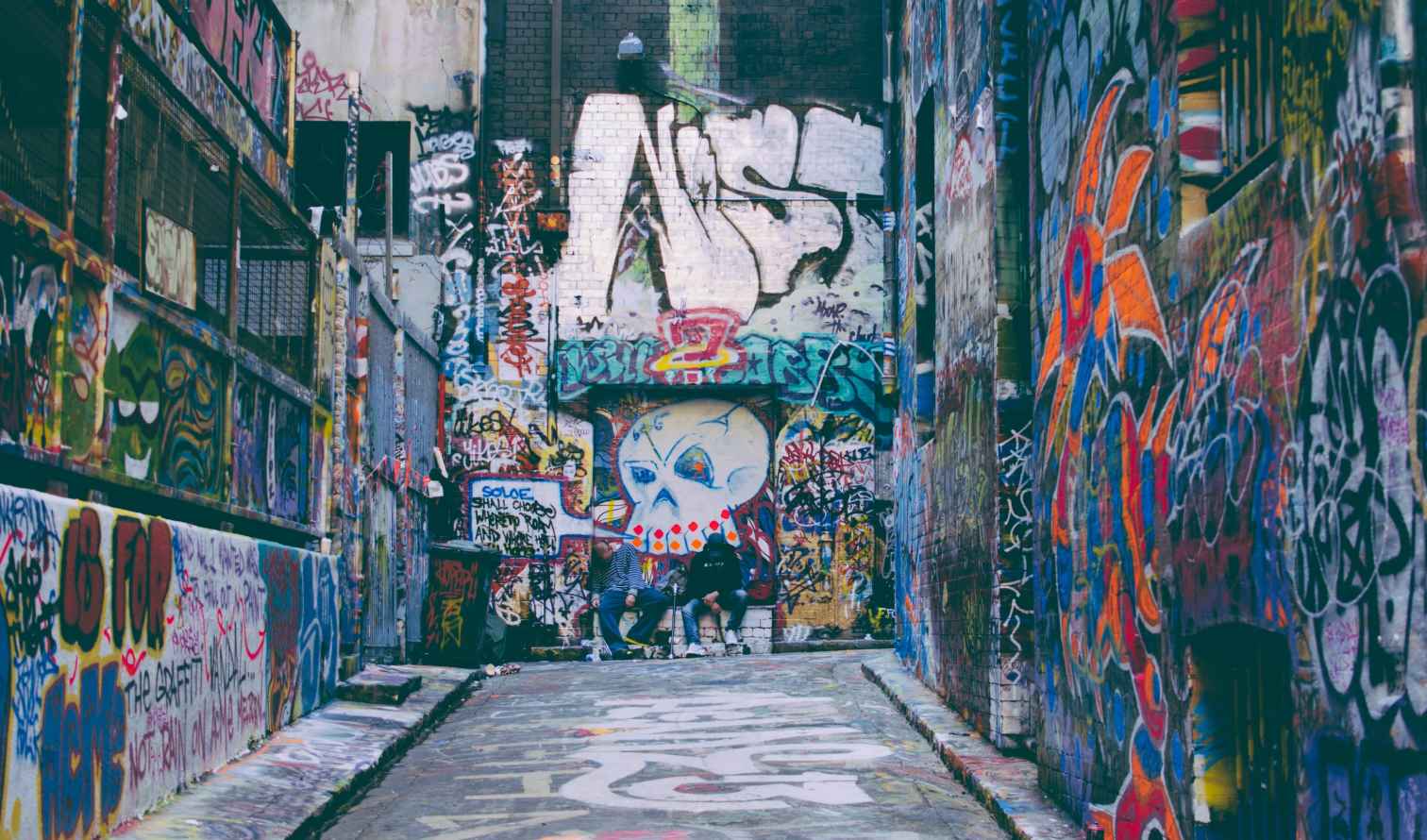 Graffiti-covered walls in Hosier Lane, Melbourne, with people sitting by the mural.