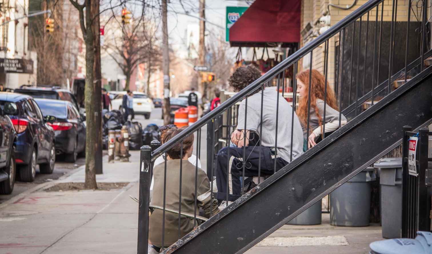 People sitting on stairs by a sidewalk in Brooklyn, New York.