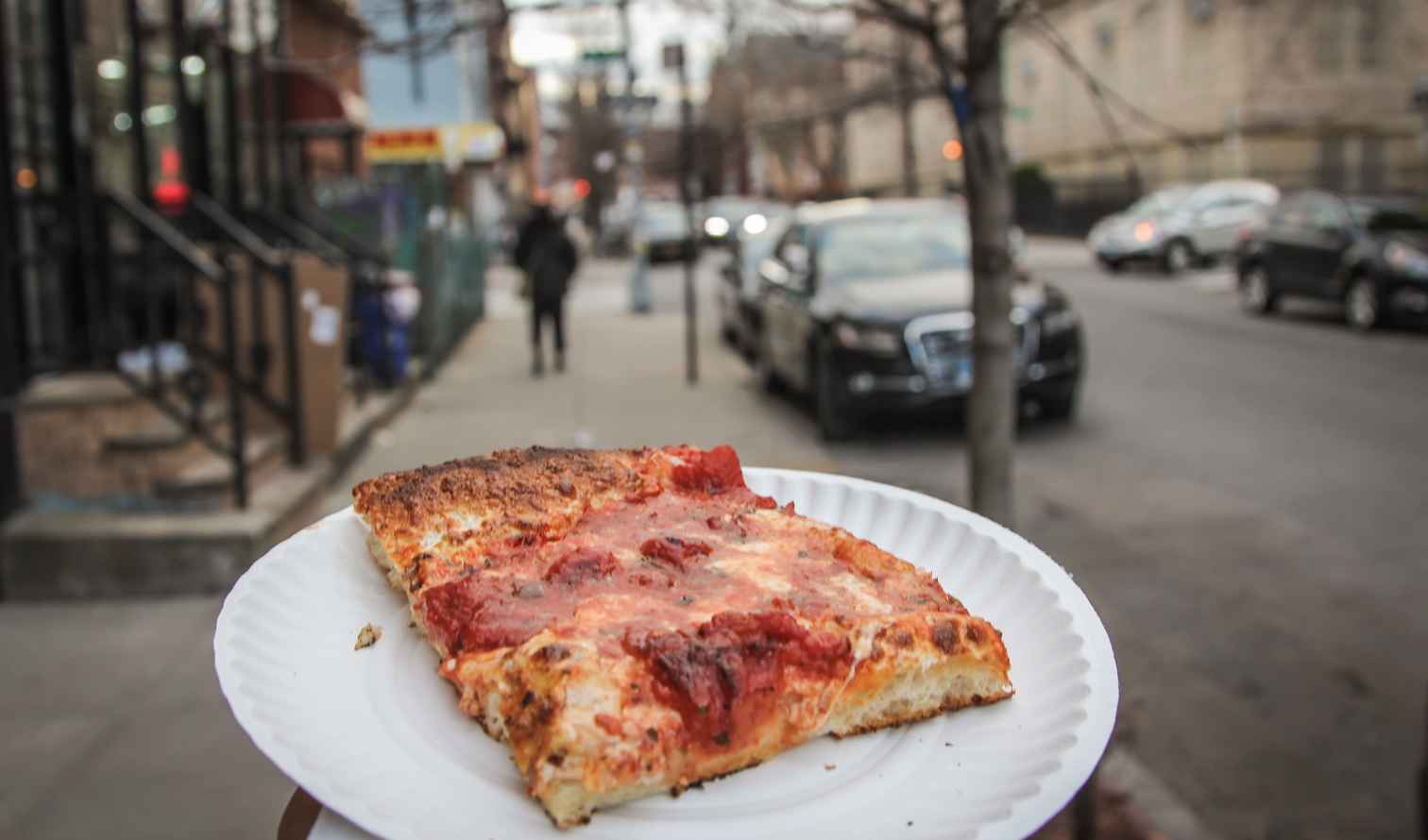 Slice of pizza on a plate held on a city street. New York