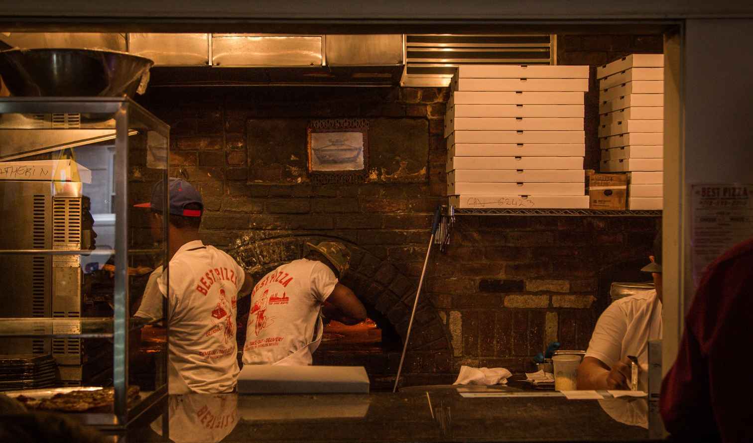 Pizza chefs working at Best Pizza, Brooklyn, behind a brick oven.