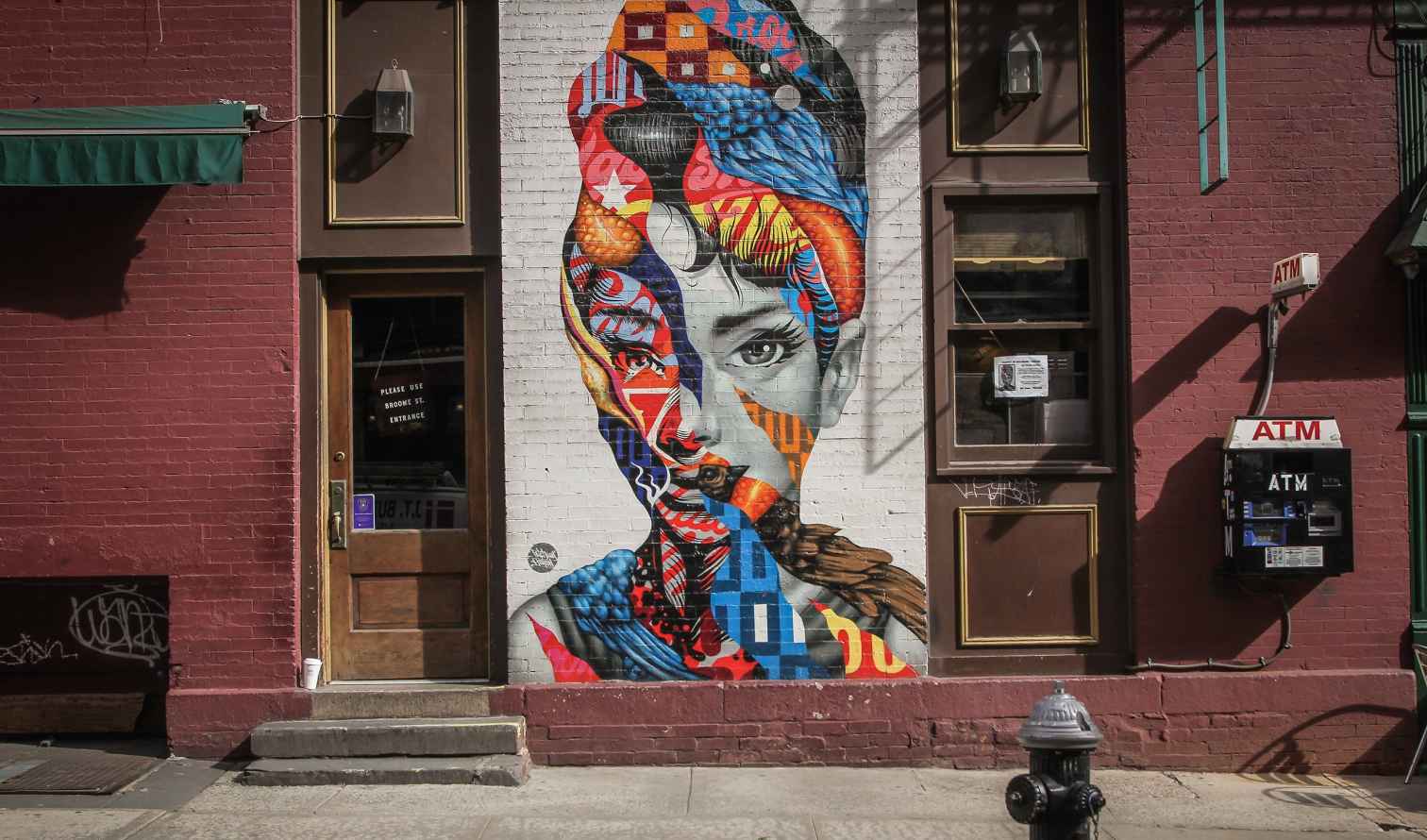 Street art mural on a brick wall beside a wooden door and an ATM in New York