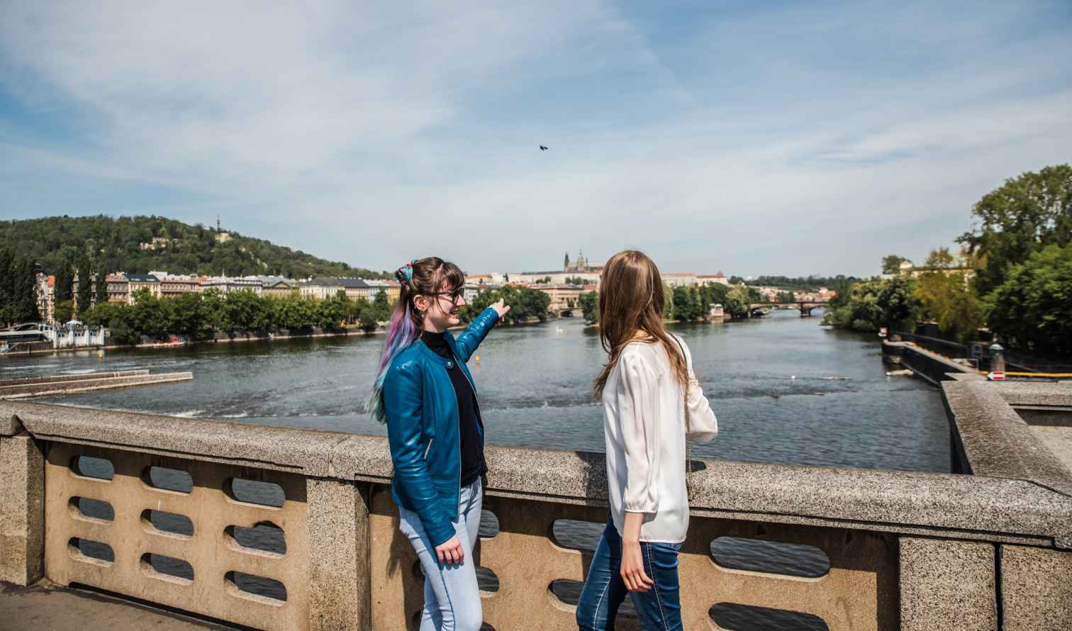 Two people on a bridge in Prague pointing towards Prague Castle.