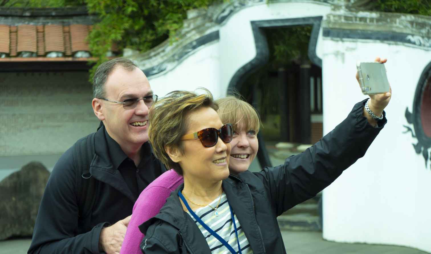 Three people taking a selfie in front of a traditional Chinese garden entrance in Taipei