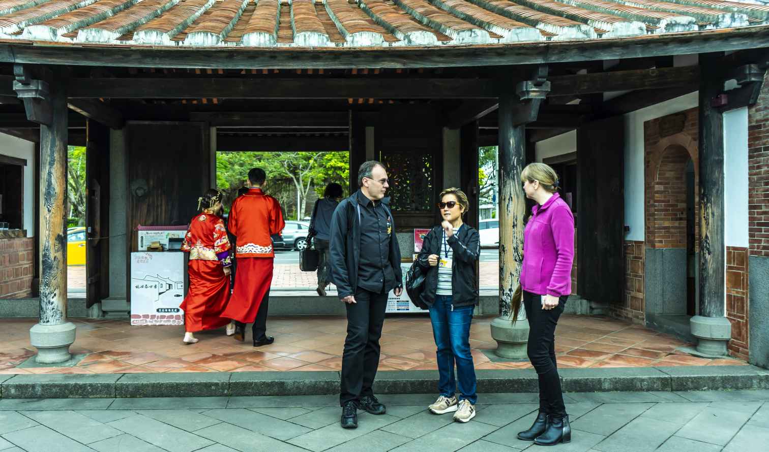 Three people talking outside a traditional tea house entrance in Taipei