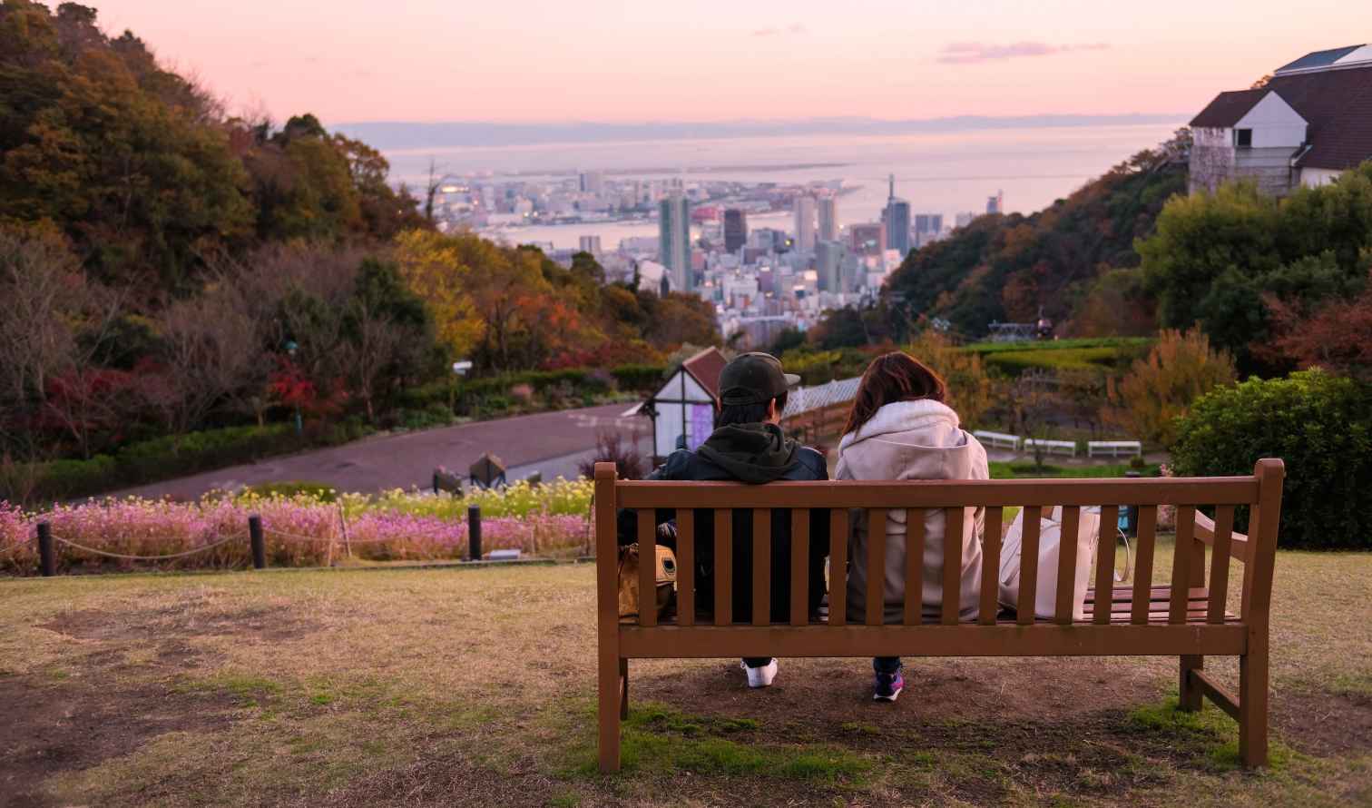 Two people sitting on a bench overlooking Kobe cityscape.