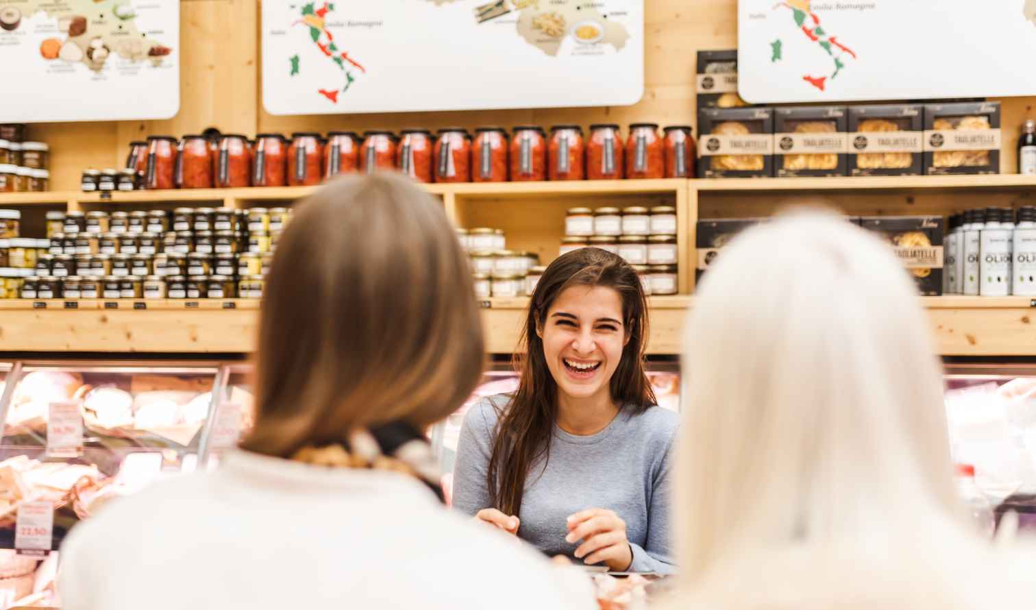 A woman interacting with two people at a deli counter in Bologna