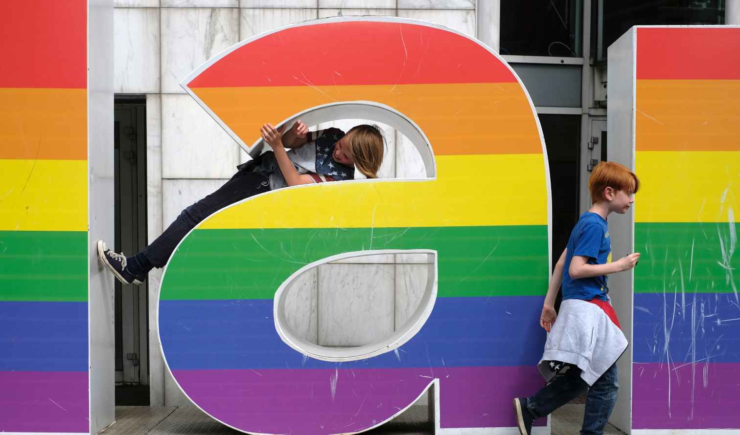 A boy climbs through a giant rainbow letter, while another walks by in Amsterdam