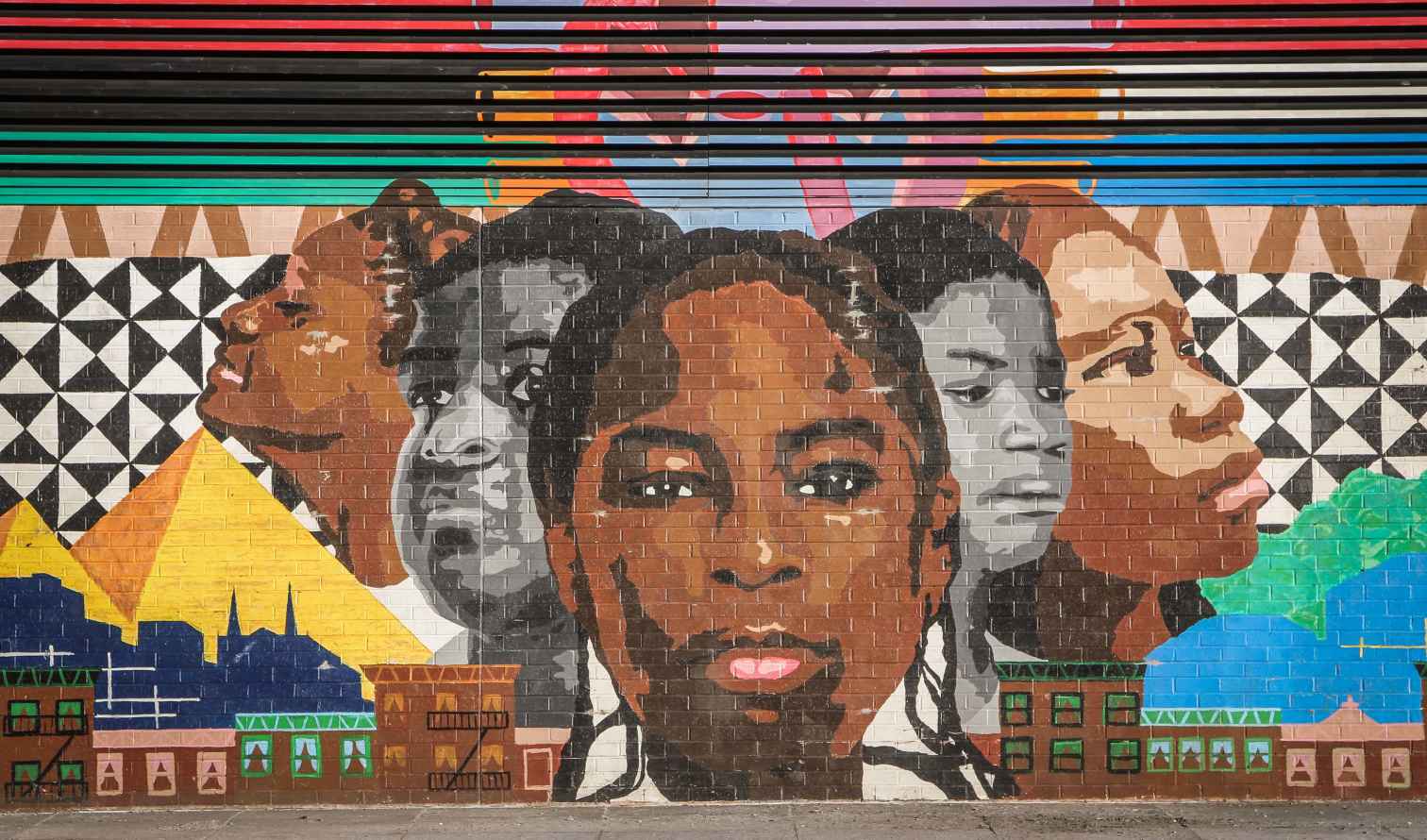 Mural on a brick wall depicting multiple faces and cultural symbols in New York