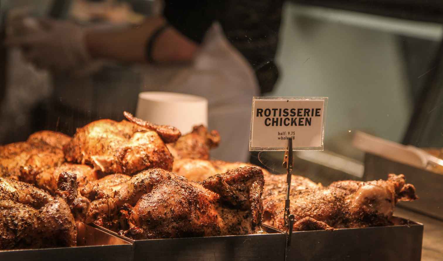 Rotisserie chickens displayed in a metal tray at a food market in New York