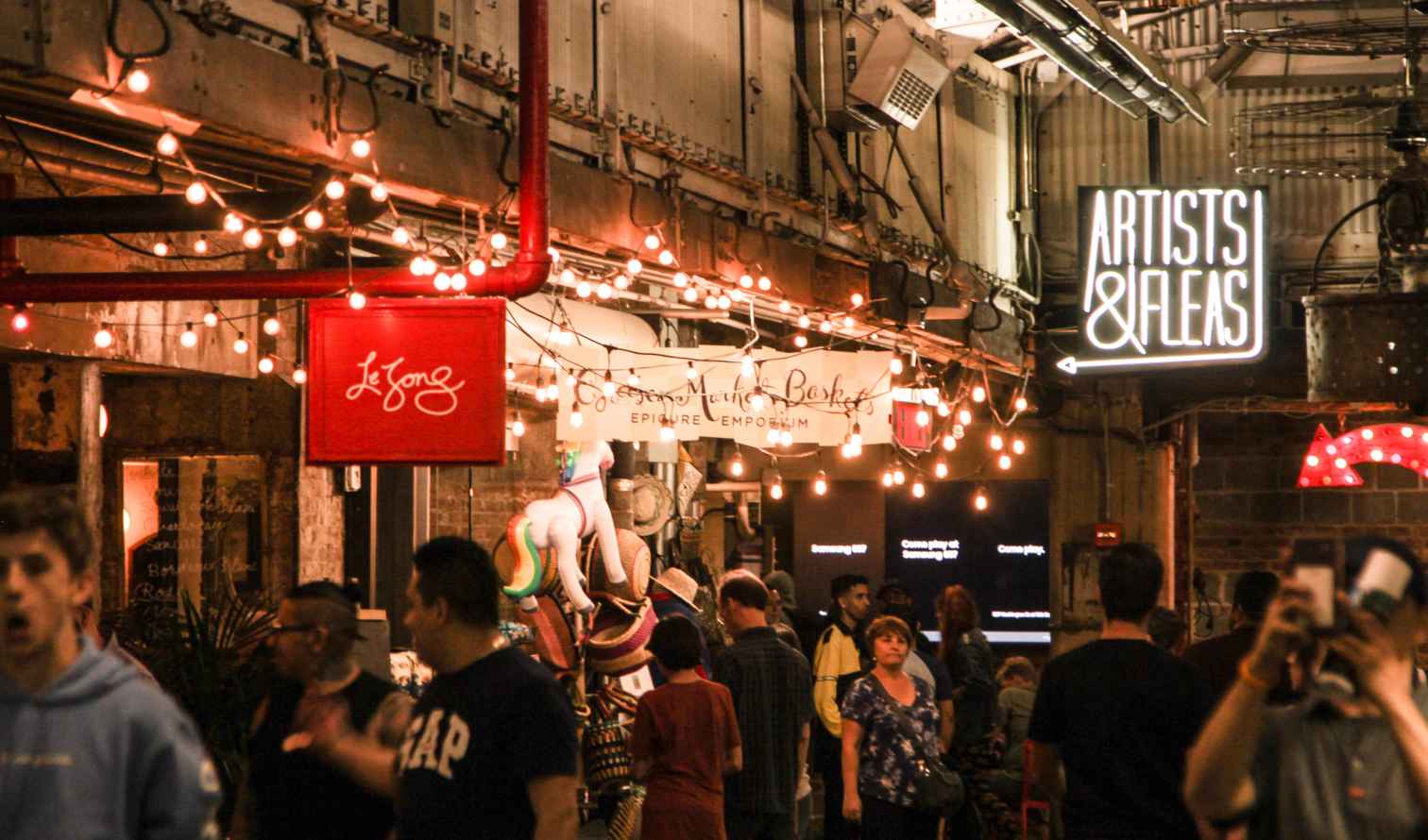 Signs for Le Song and Artists &amp; Fleas above a busy market alley in New York