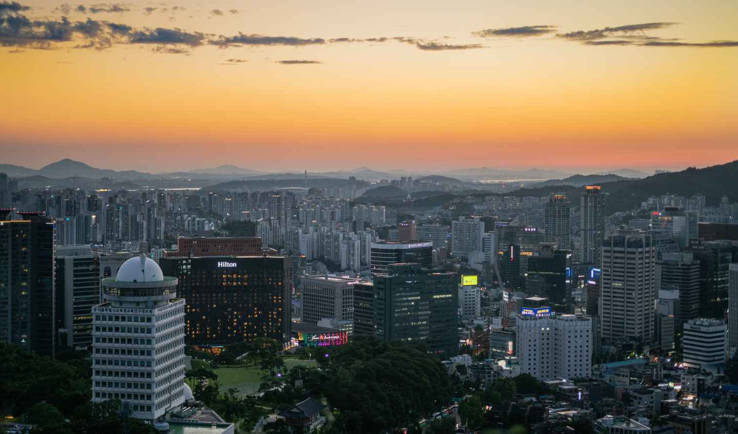 Seoul cityscape at sunset with mountains in the background.