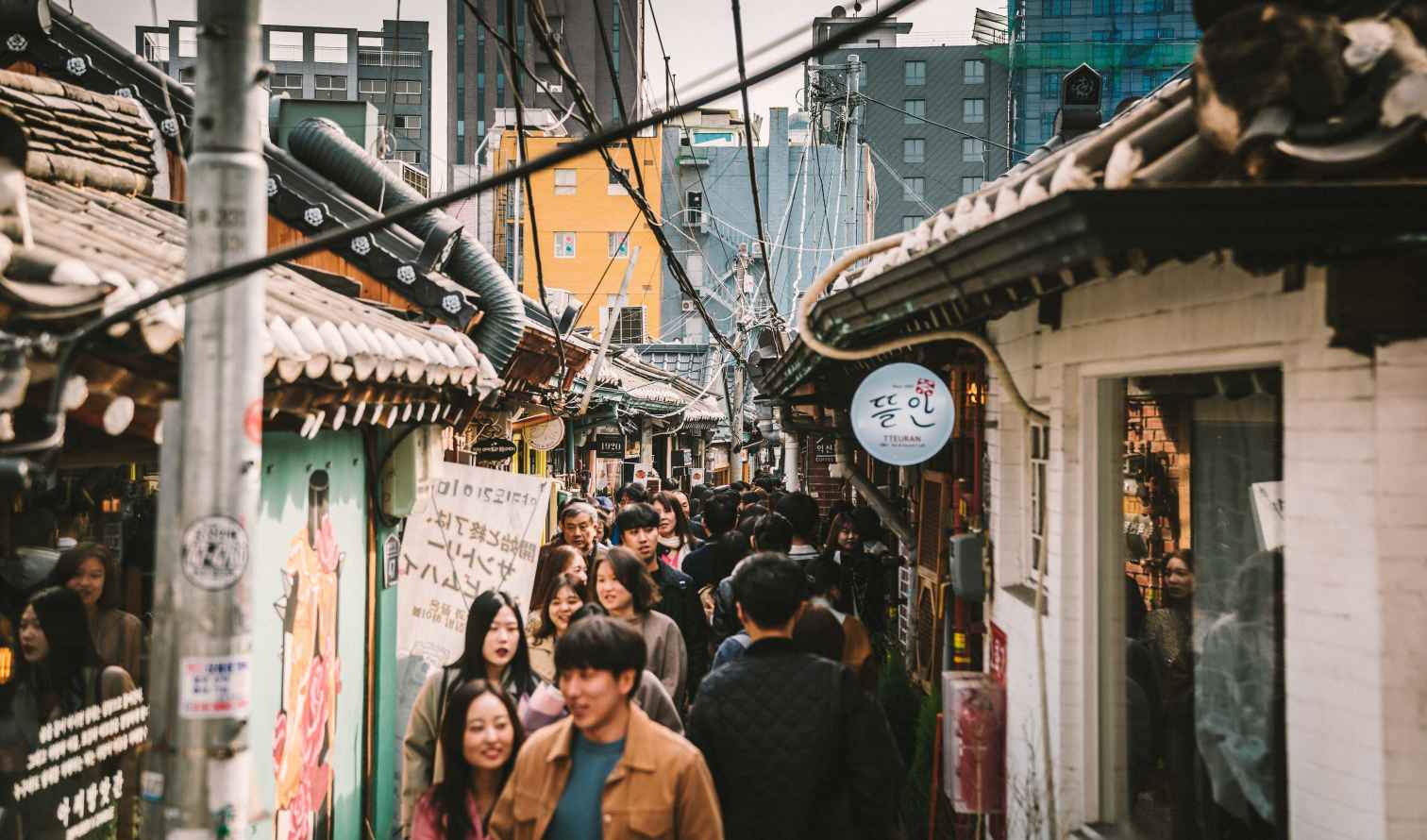 People walking in Ikseon-dong Hanok Village, Seoul, with traditional roofs visible.