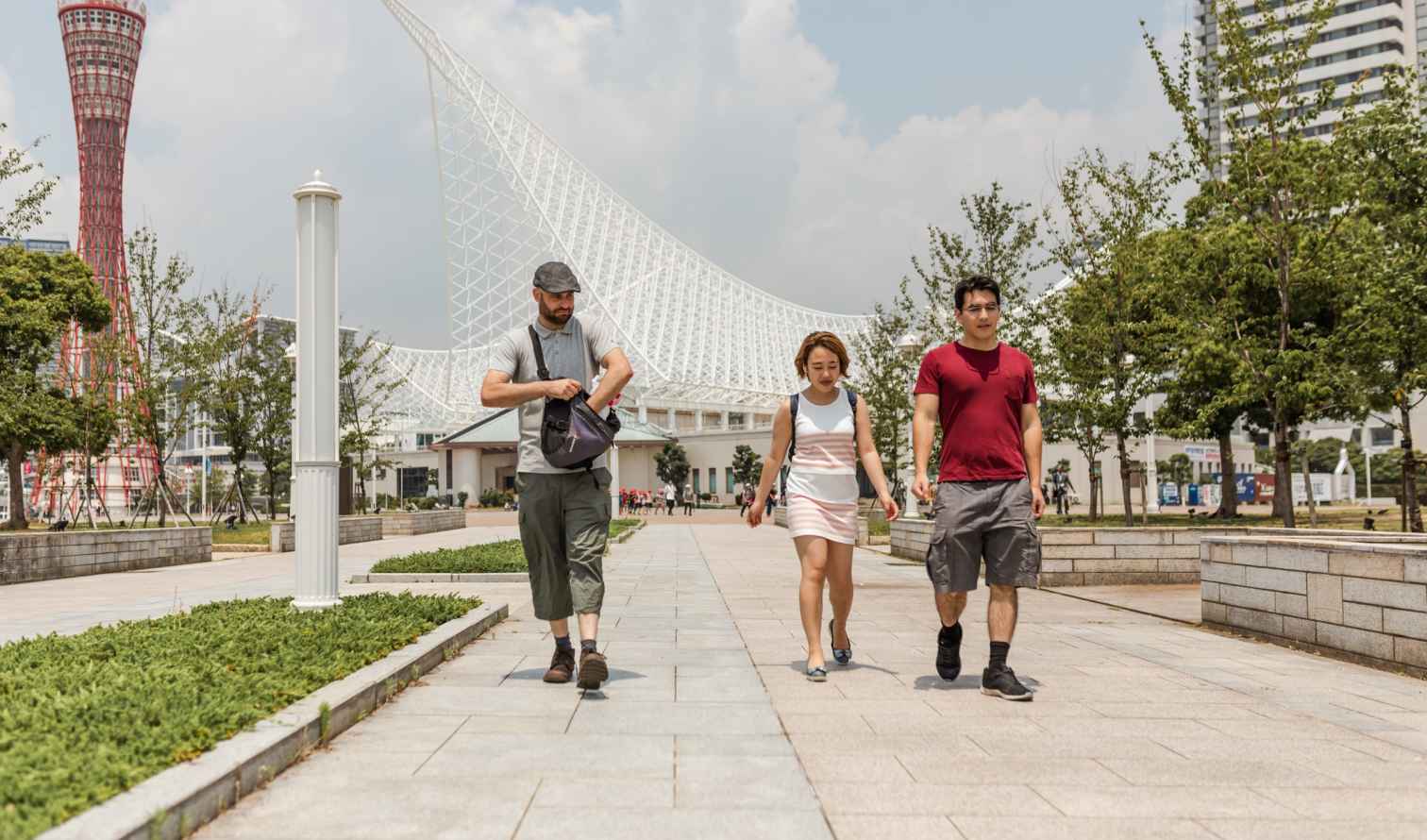 Three people walking near Kobe Port Tower and Maritime Museum in Japan.