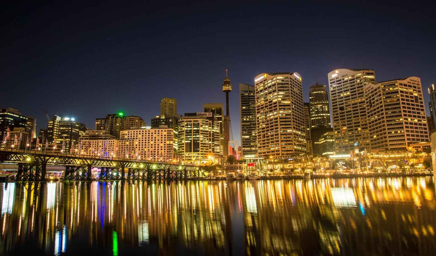 Sydney skyline with illuminated skyscrapers reflecting on the water at night.