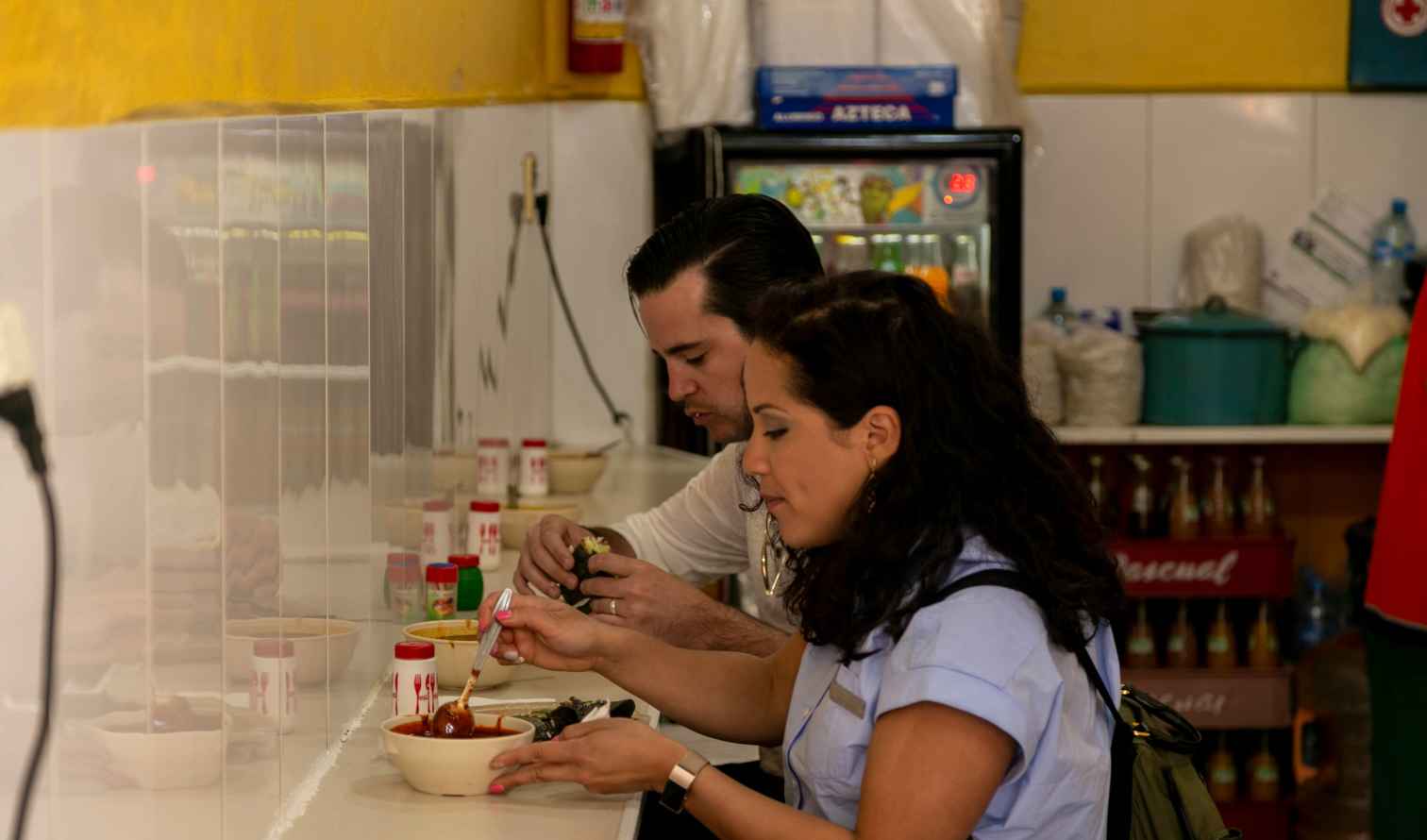Two people eating at a counter with a yellow wall in Mexico City